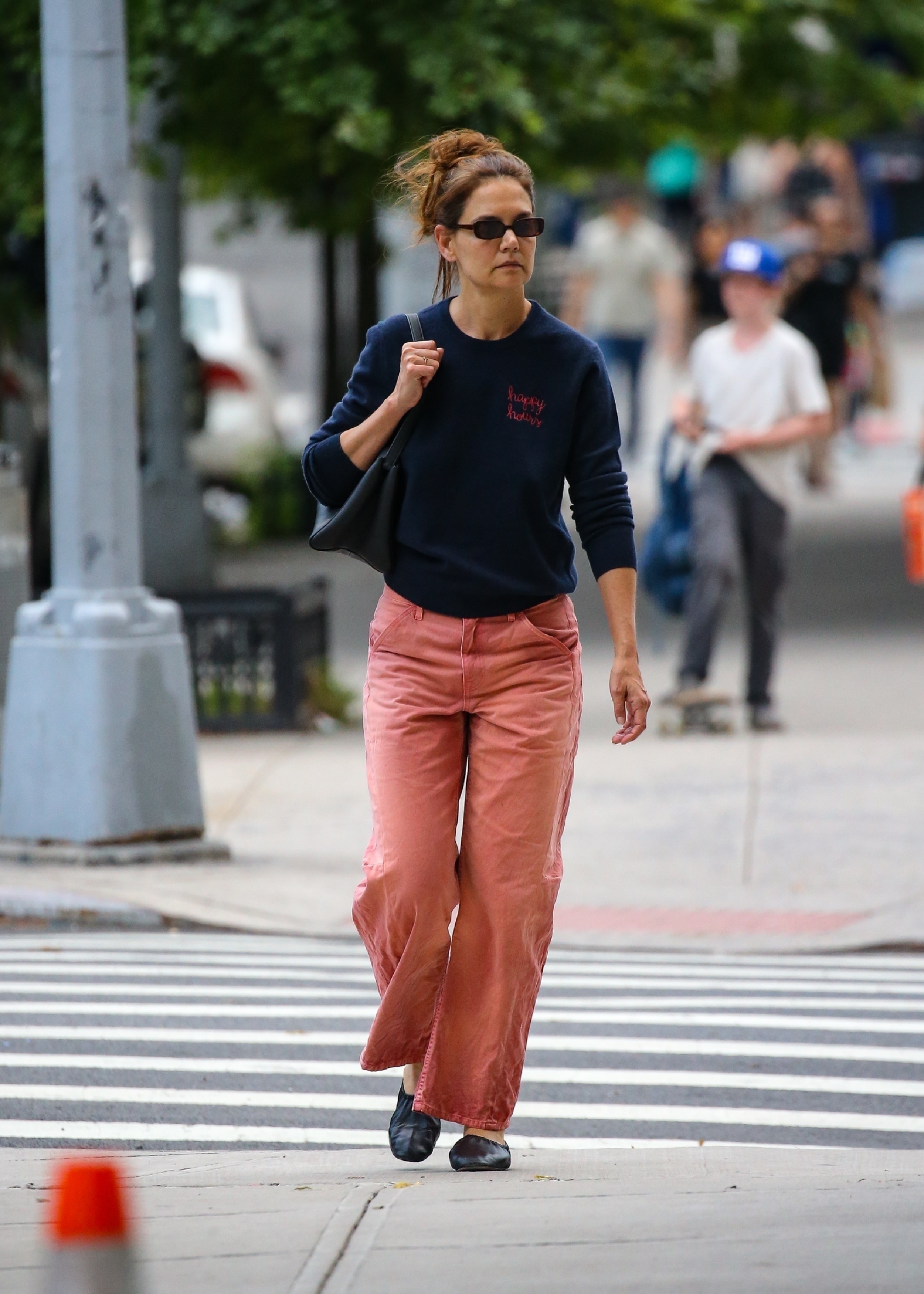 Katie Holmes carries a black Khaite bag and wears a navy sweatshirt featuring the words Happy hours