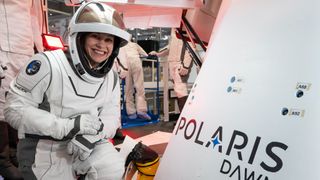 anna menon in a spacesuit beside a crew dragon