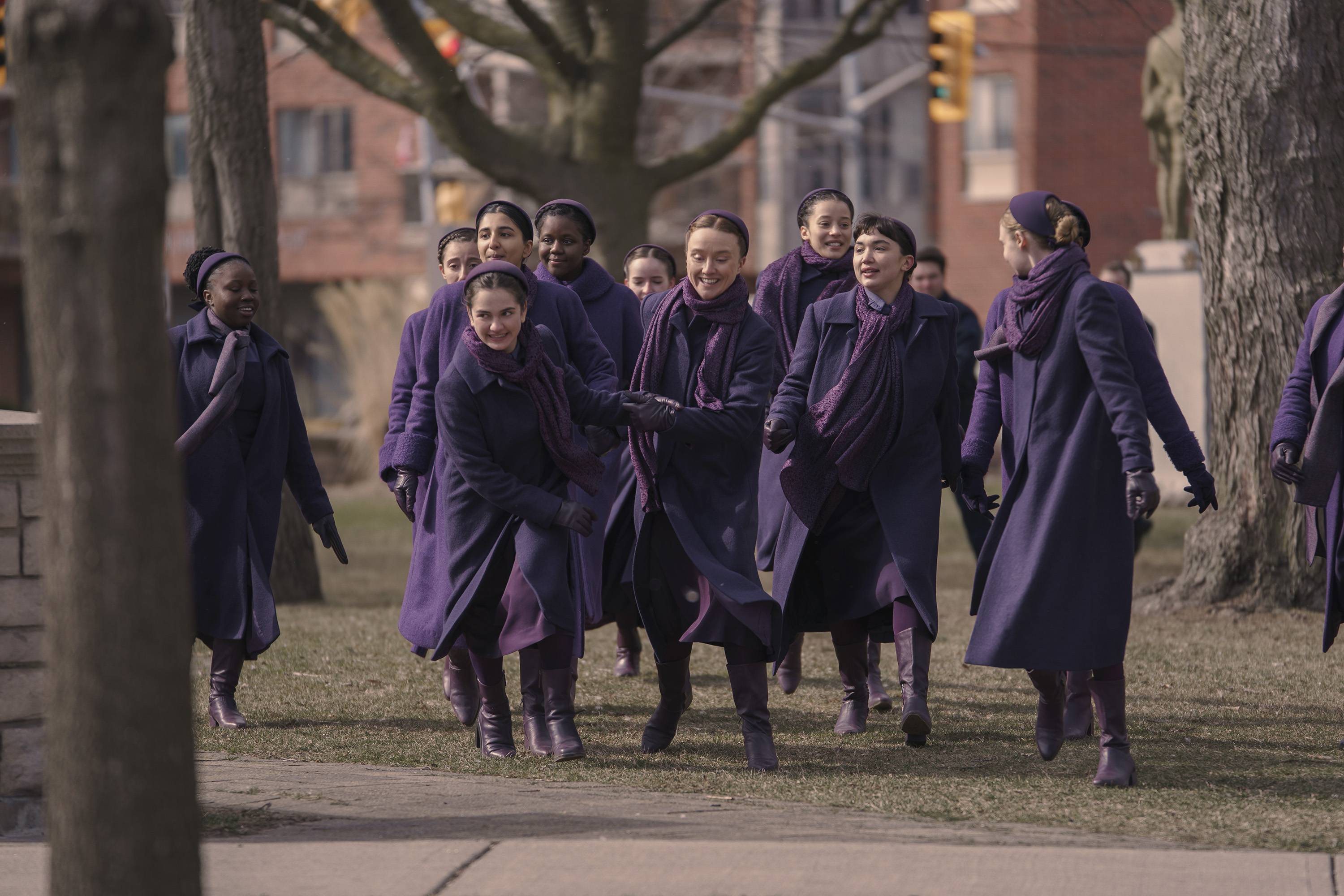 a handful of commanders daughters dressed in purple run through the field outside of school including SHECHINAH MPUMLWANA, BIRVA PANDYA, MATTEA CONFORTI, ELLEN OLIVIA, CHASE INFINITI, ROWAN BLANCHARD