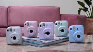 The Fujifilm Instax Mini 12 on a table with each of its five color choices