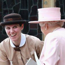 Nanny Maria smiling and talking to Queen Elizabeth, wearing a pink hat and coat