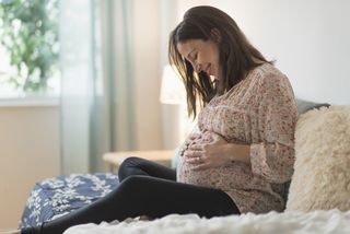 Pregnant woman sitting on a bed.