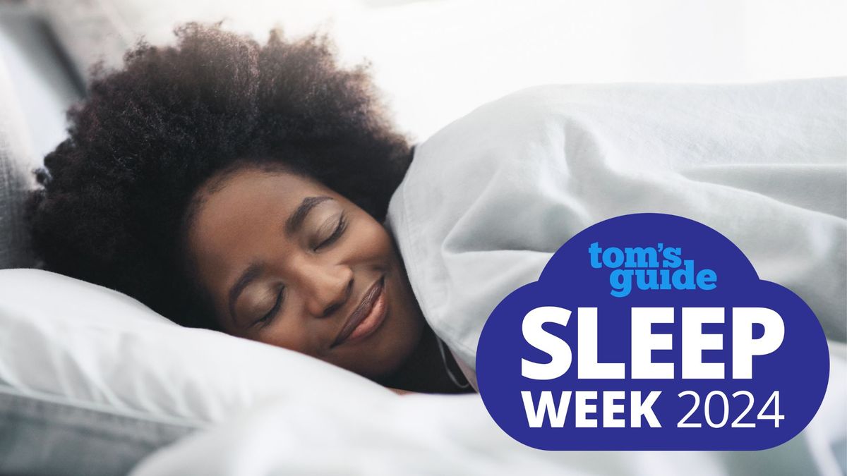 A woman with dark curly hair closes her eyes and smiles as she lays her head on a white pillow and pulls a white duvet up to her chin. A Tom&#039;s Guide Sleep Week 2024 logo is placed over the top of the image.