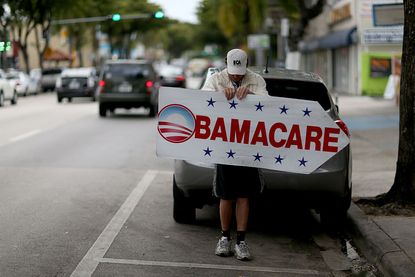 A man holds a sign directing people to where they can sign up for healthcare under the Affordable Care Act.