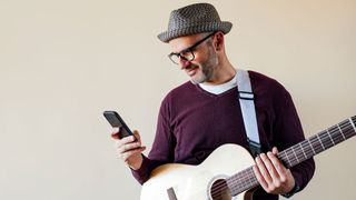 Man using smart phone and holding an electroacoustic guitar.