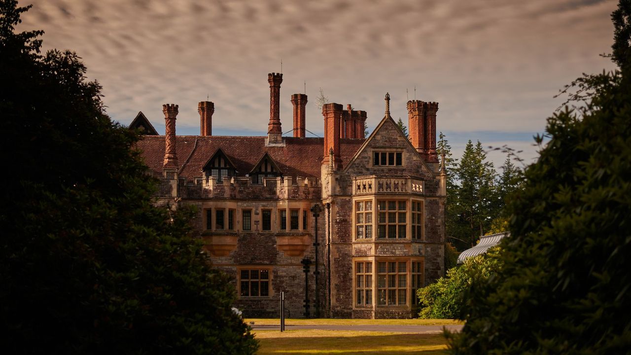 Rhinefield House Hotel with clouds in the background and trees lining the sides