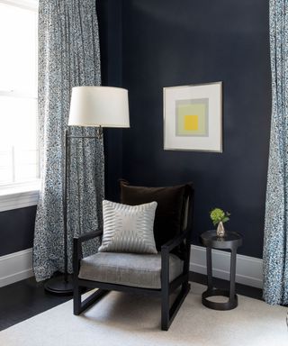Corner of living room, blue painted walls, dark gray and black armchair, blue patterned curtains