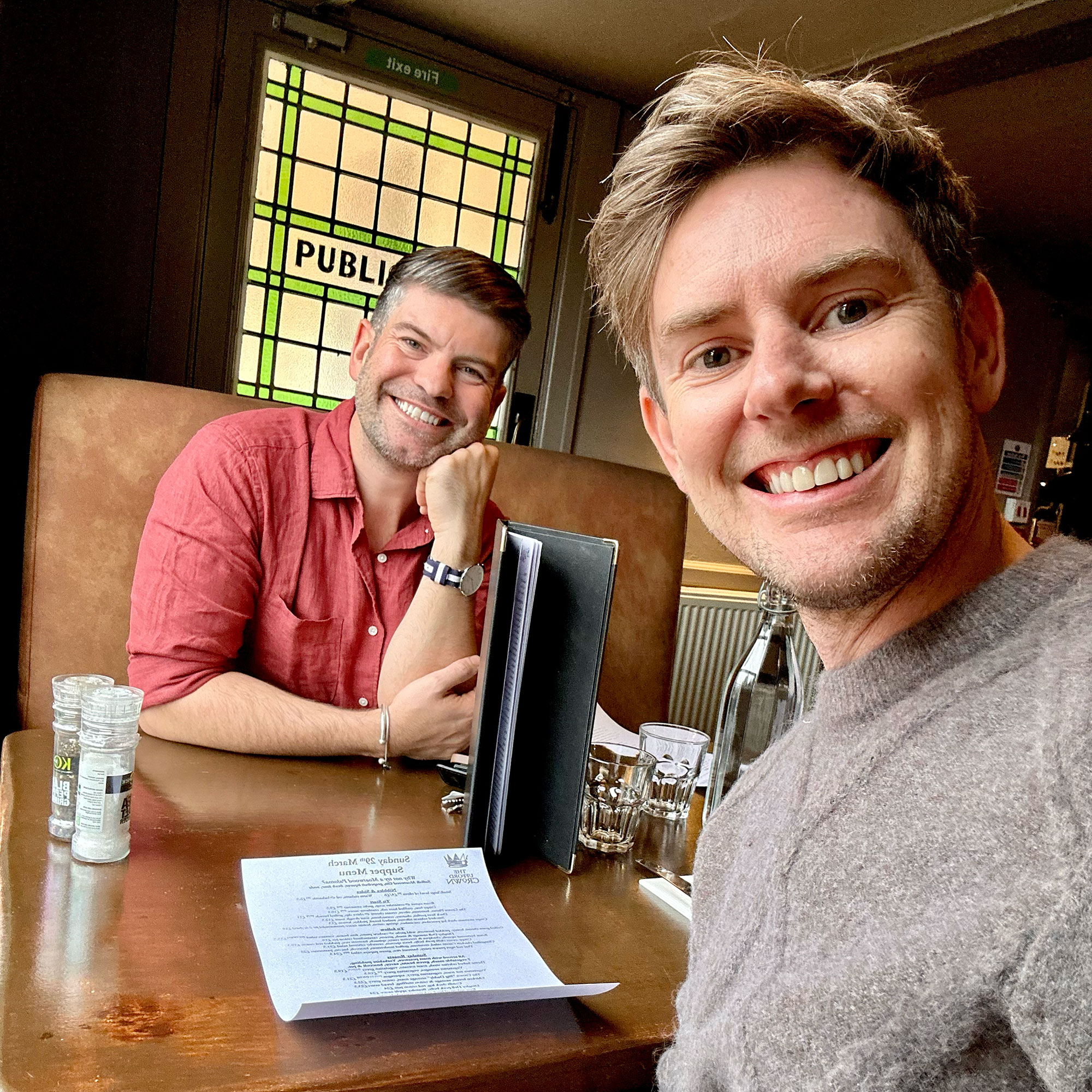 Two men at a pub table, one taking the selfie