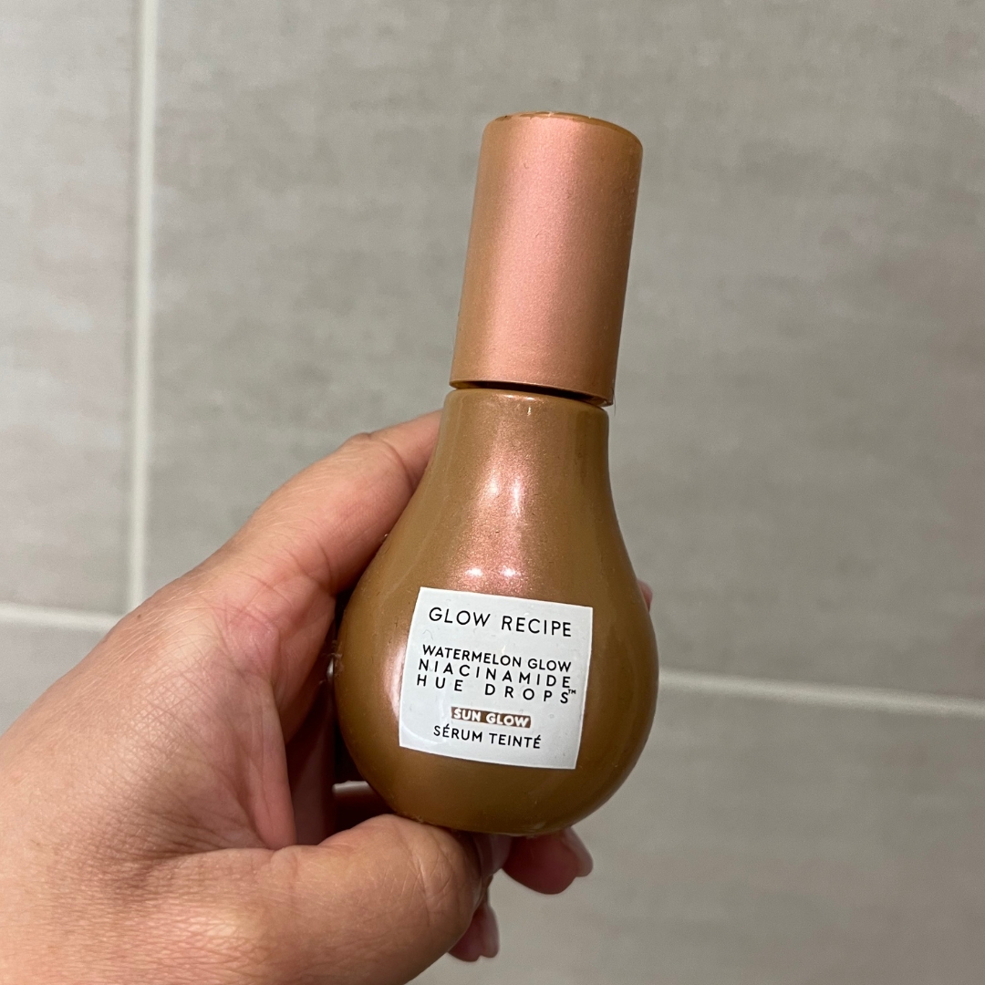 Hand holding brown bottle of Glow Recipe Watermelon Glow Niacinamide Hue Drops Tinted Serum in Sun Glow