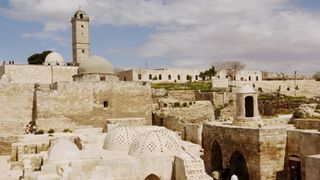 A view of the ancient citadel in Aleppo, Syria, with domed buildings and a tower.