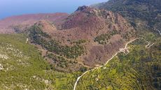 An aerial view of Methana volcano, a large peak in the middle of a lush landscape.