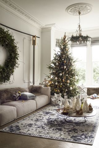 A large living room with a tall Christmas tree decorated with neutral colored ornaments