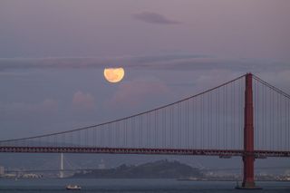 a bright full moon above a red suspension bridge