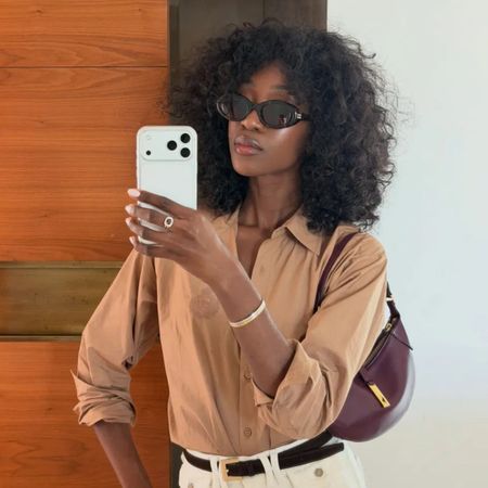 A woman taking a mirror selfie with dark brown, curly hair