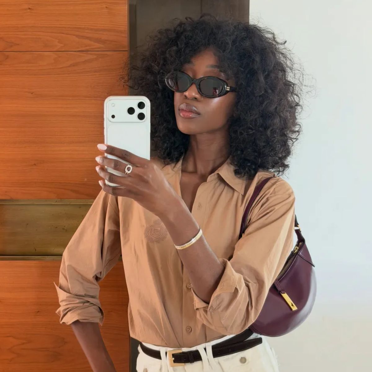 A woman taking a mirror selfie with dark brown, curly hair