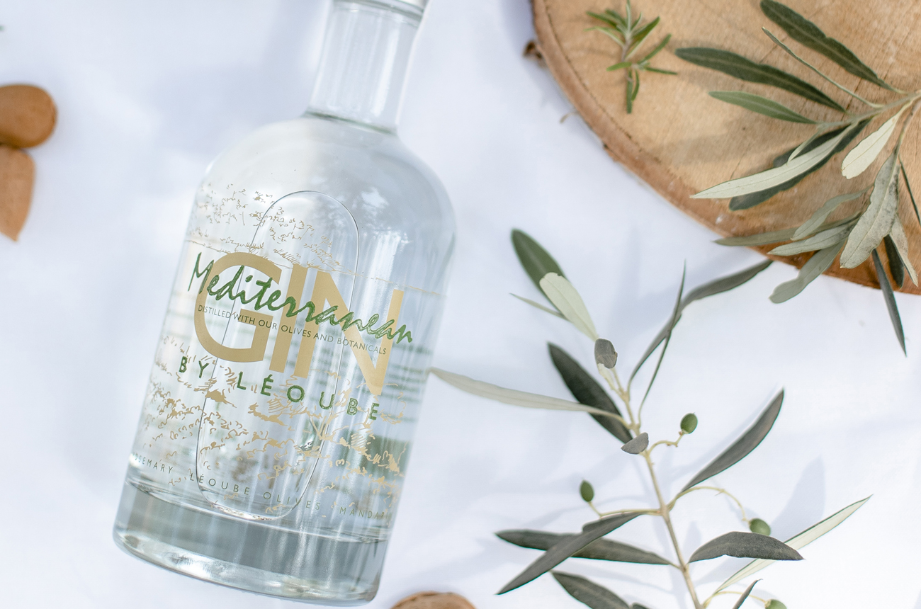 A bottle of gin on a table top with olive branches