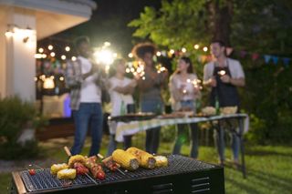 A happy group of friends enjoying a barbeque in the evening with delicious food and sparklers.