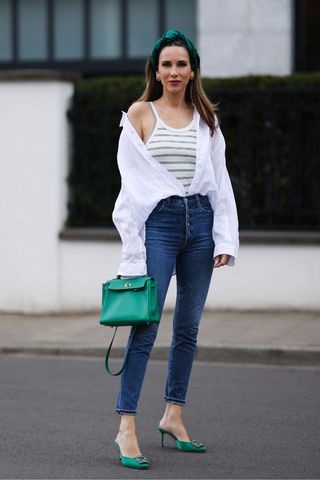 A woman wearing a relaxed white shirt, denim jeans and green accessories