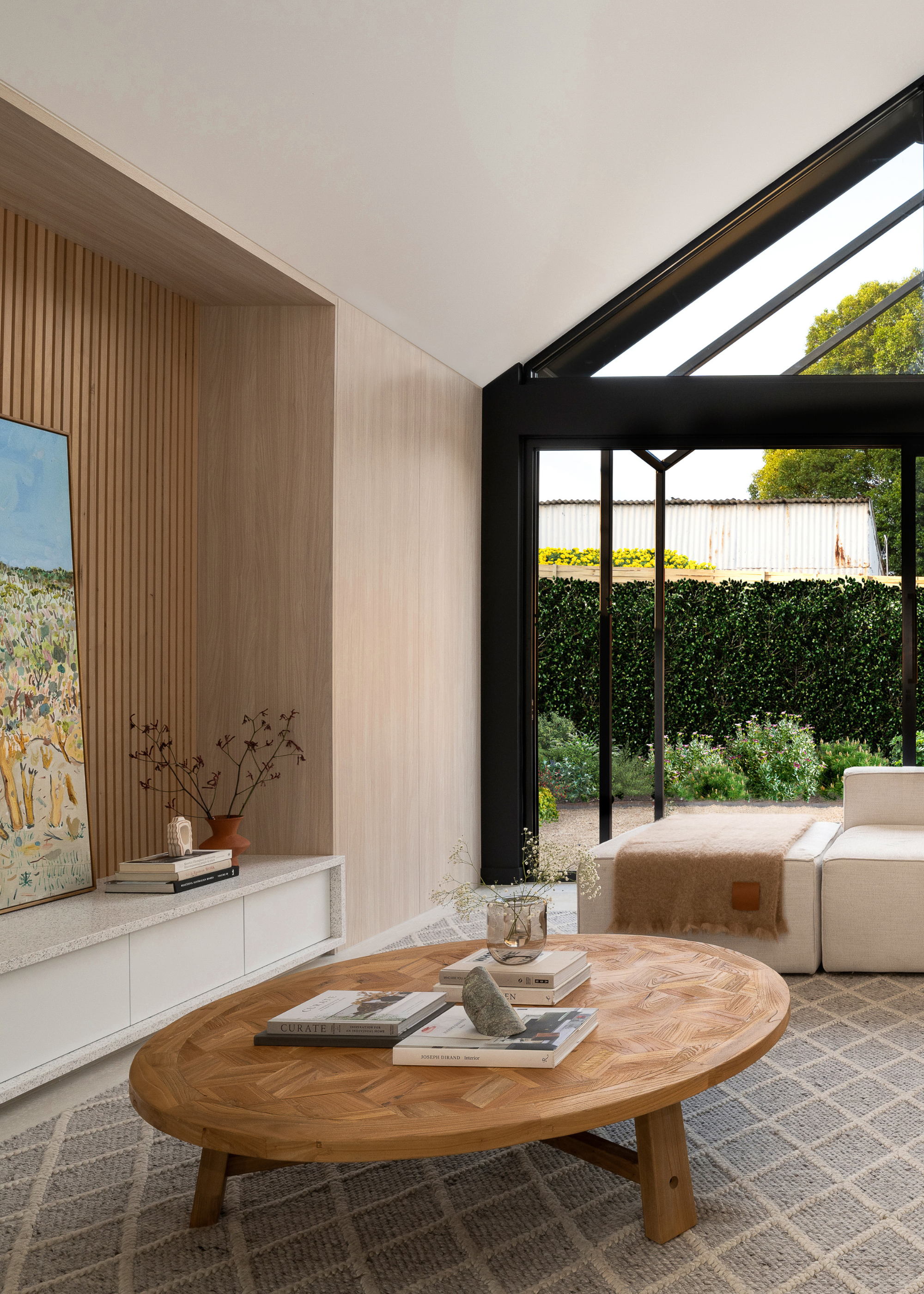 A living room with a textured area rug, a round wood coffee table, a beige couch, a fringed throw and glass doors leading to a backyard