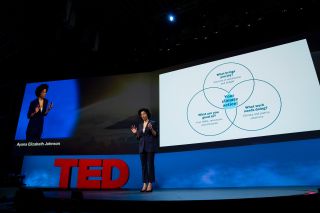 Ayana Elizabeth Johnson in a dark-colored pantsuit standing on TED talk stage