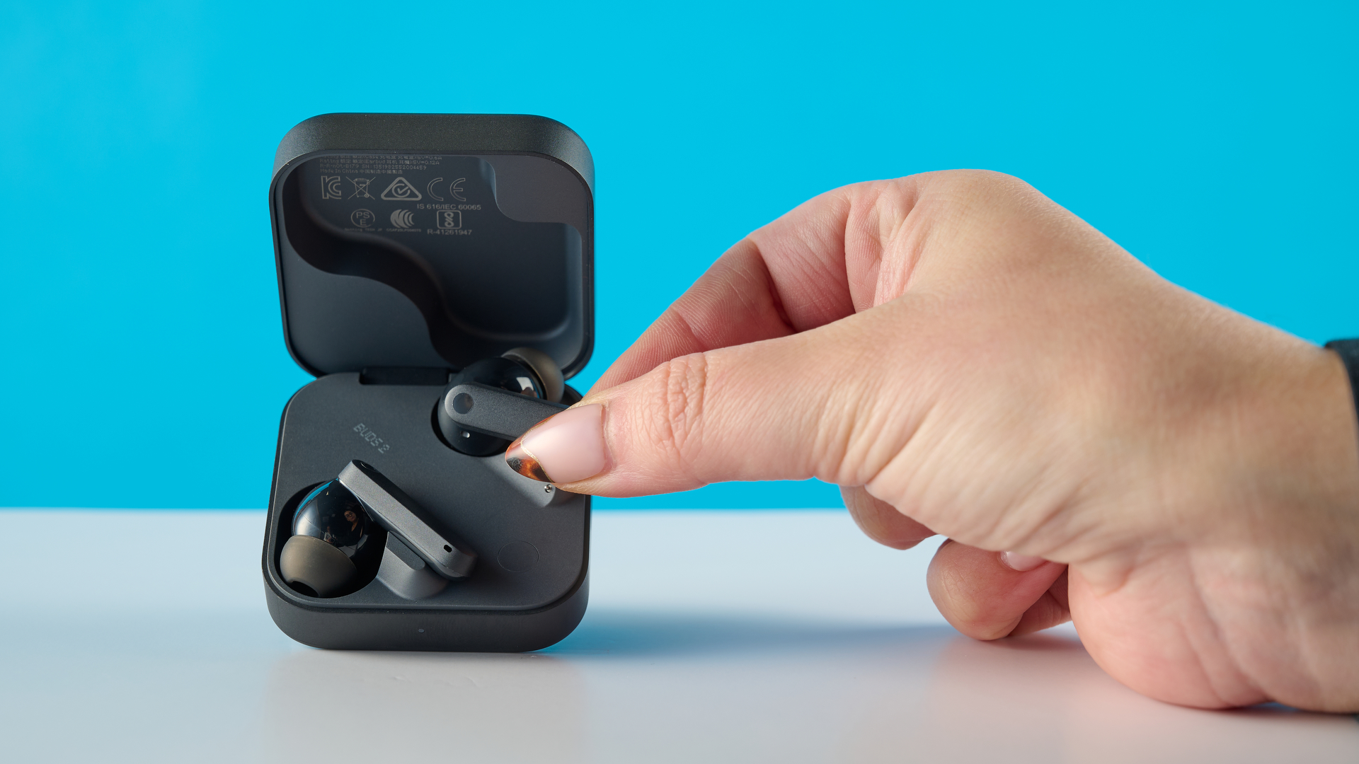 CMF Buds 2 in Dark Gray photographed on a gray table in front of a blue background