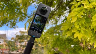 Insta360 X3 360 camera on a stick in front of some trees