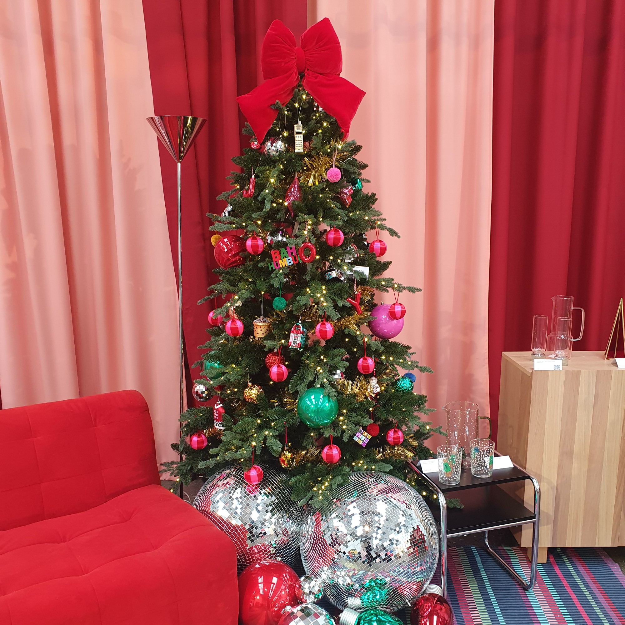 A Christmas tree at the Habitat Christmas press show decorated with colourful baubles and a big red velvet bow tree topper