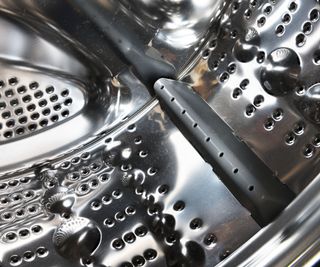 The inside of a clean silver front loading washing machine drum with grey plastic baffles