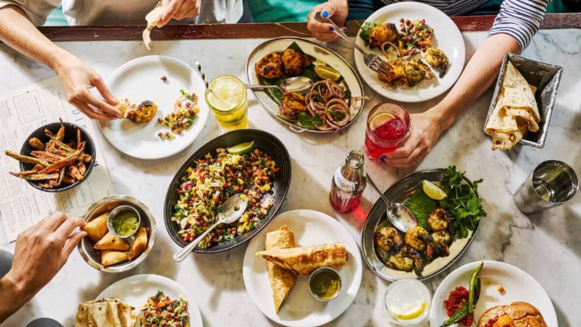 an aerial image of a table of food at dishoom, with four people around the table eating