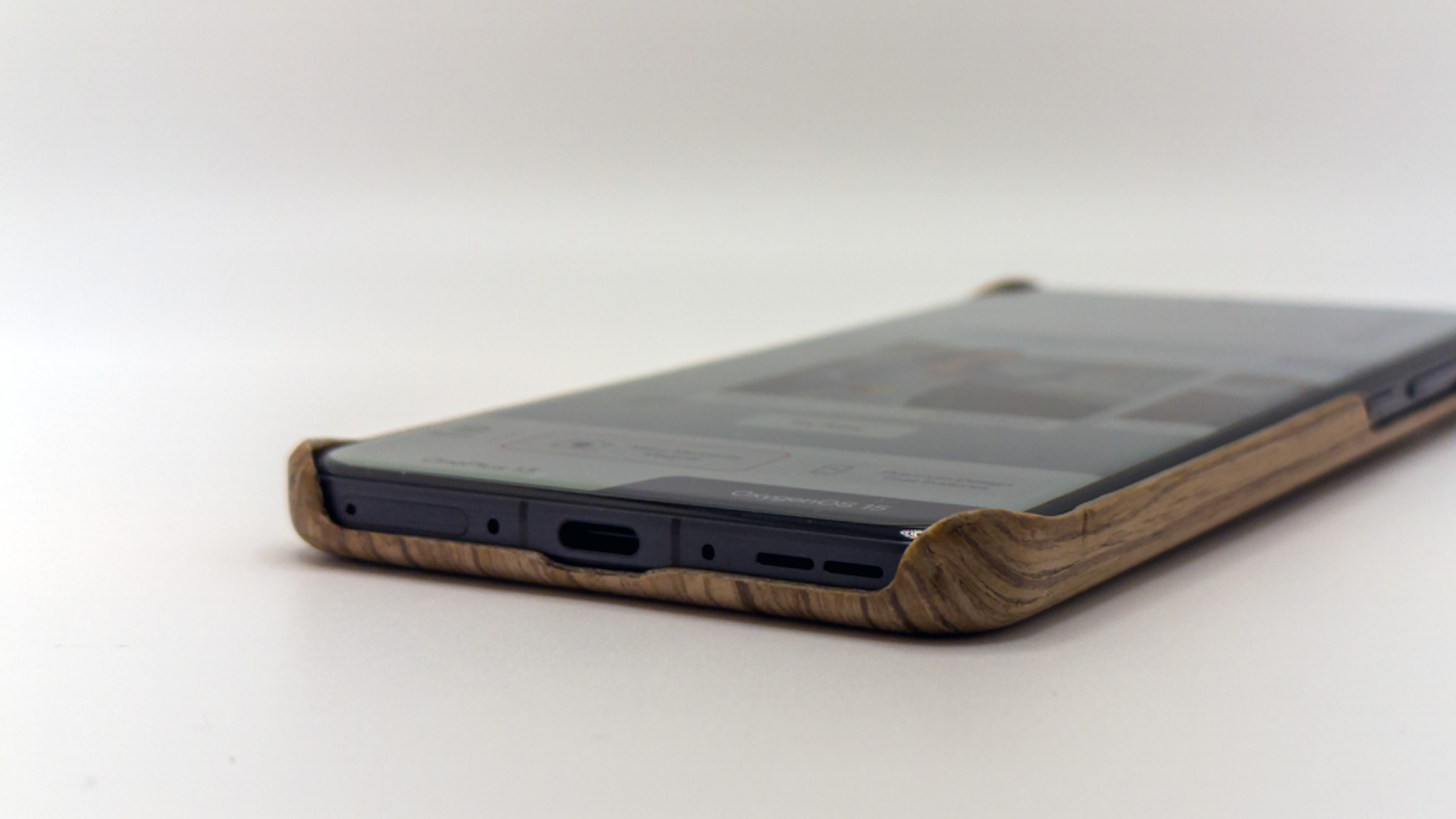 The bottom edge and covered corners of the official OnePlus 13 wood case