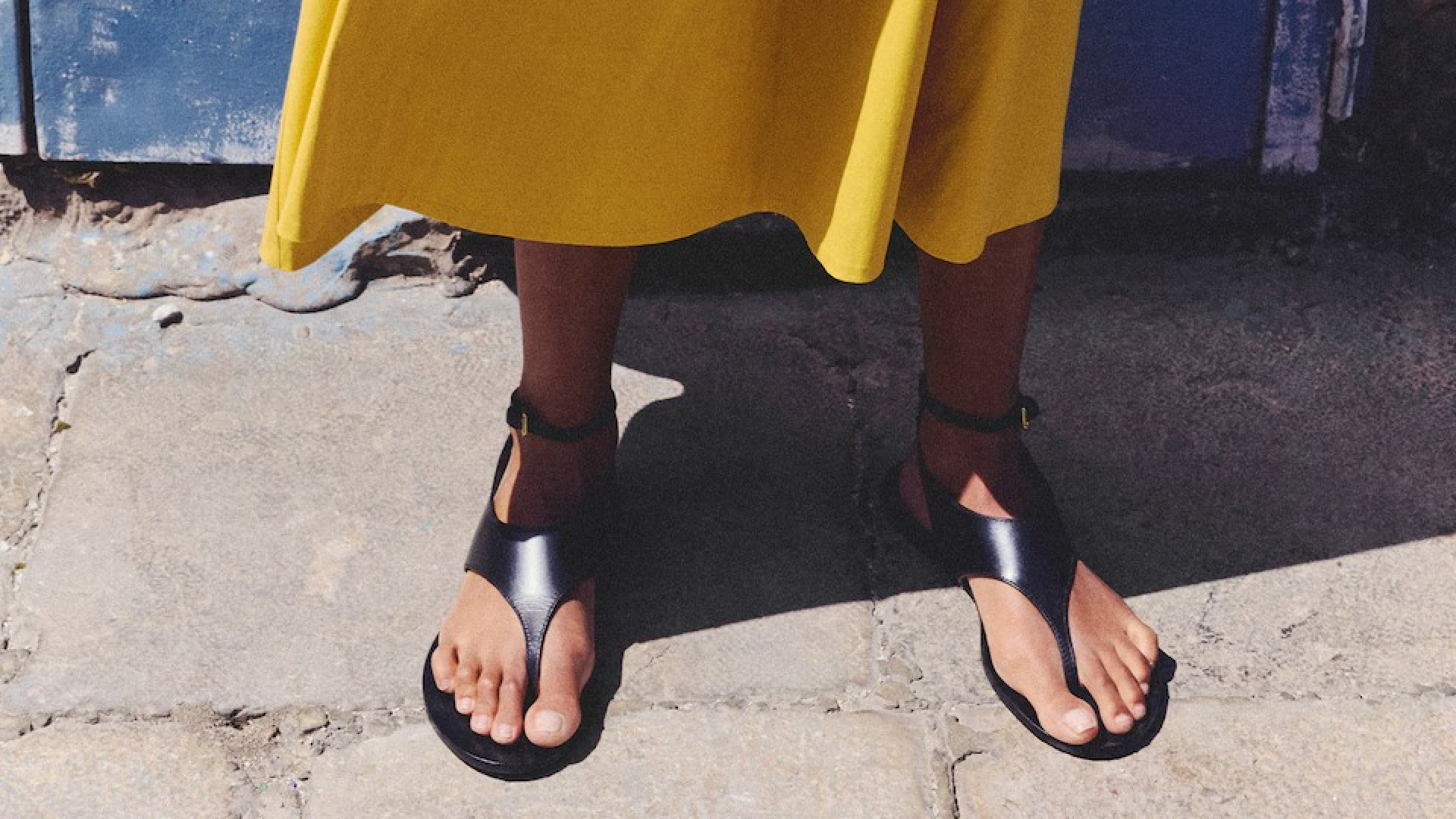 Model wearing mango Leather Straps Sandals with yellow skirt on coblestone street
