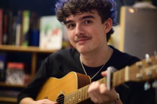 Viltrox AF 85mm F1.4 Pro lens sample gallery: young man holding a guitar in a living room at night