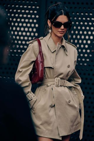 Kendall Jenner at Milan Fashion Week Spring 2025 in a classic, cropped tan khaki trench coat and red Gucci handbag.