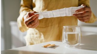 Woman's hands folding out HRT information leaflet with water and tablets sitting on the counter