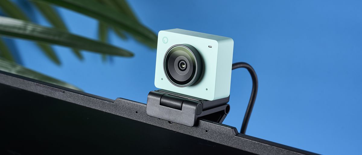 a photograph of a 1 inch wide mint webcam with a 4K sensor and built-in microphone, photographed against a blue background