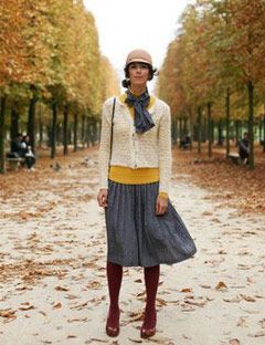 woman in parisian look clothing standing in a park with fall trees and leaves