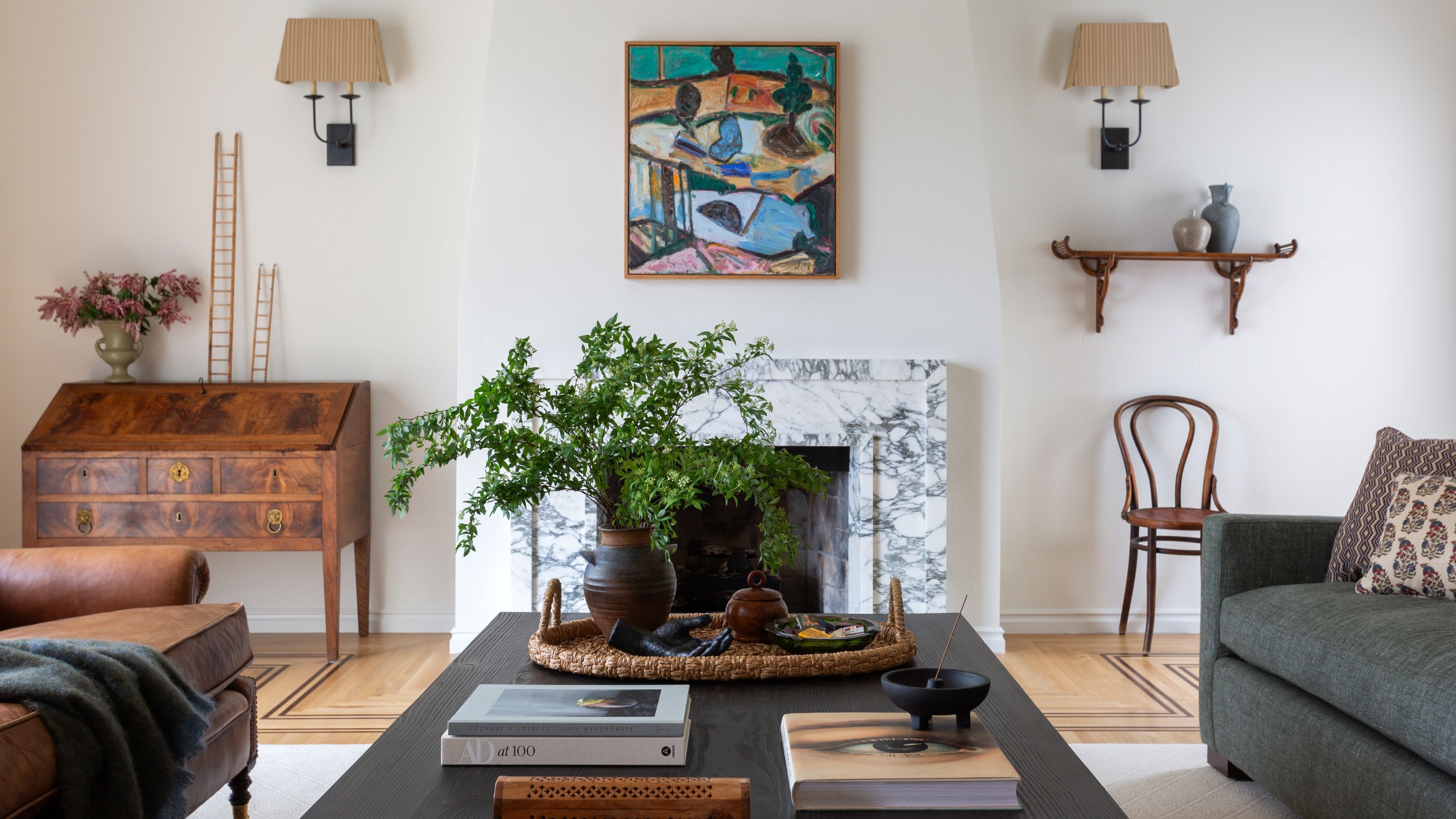 an LA living room with a marble fireplace and lots of vintage pieces including an antique French desk, vintage artwork, shelves and a small wooden chair