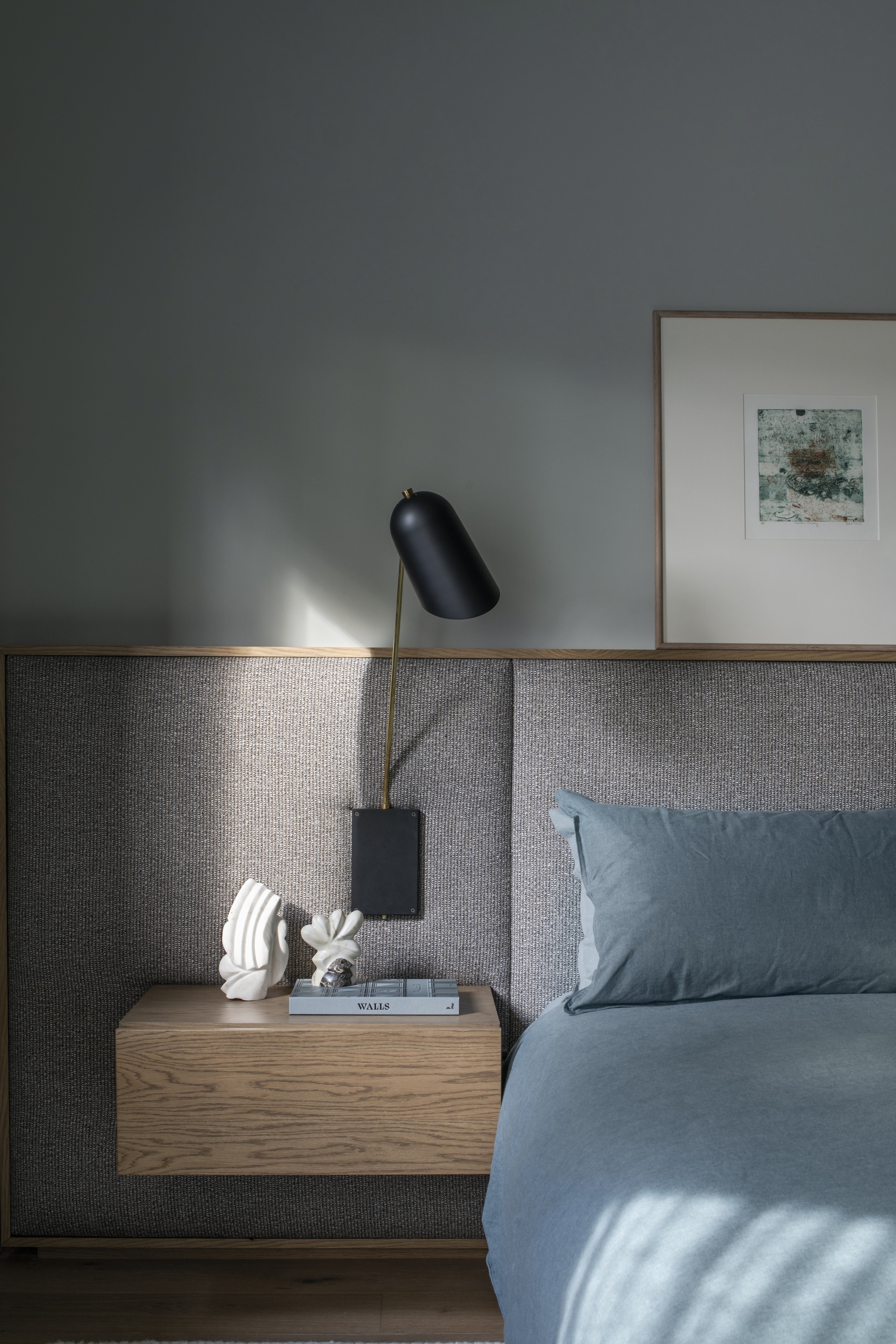 mid-century modern bedroom with light blue walls, blue bedding, built-in gray upholstered bedhead with timber floating side tables, decor, and a pendant light