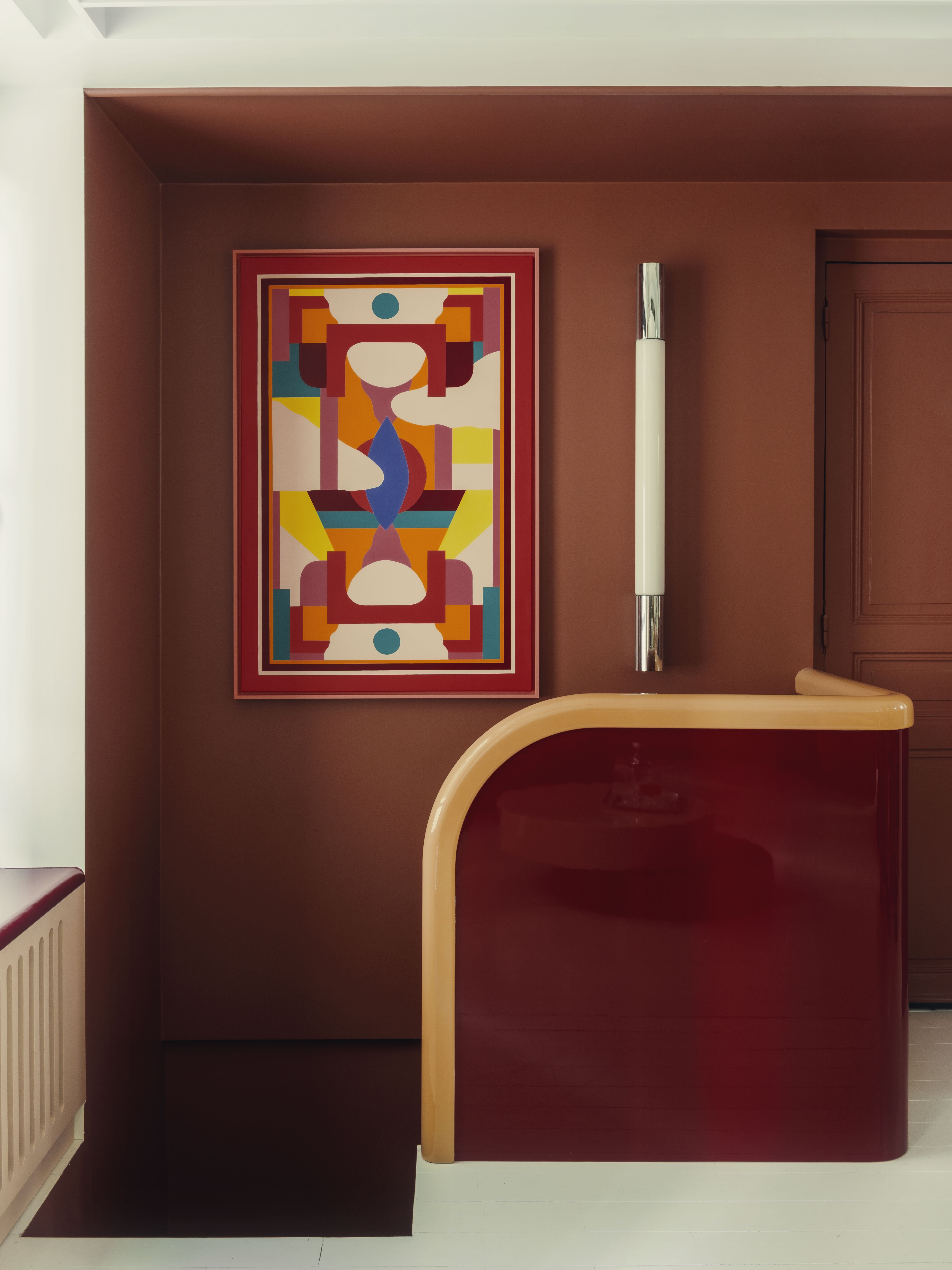 A stairwell with a red banister with a lacquer finish, backed by a colorful abstract artwork.