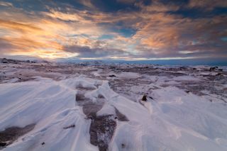 aerial view of the sun setting through clouds over icy tundra