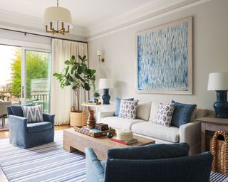Blue and cream living room with gray sofa, blue armchairs, blue artwork, wooden coffee table, plants