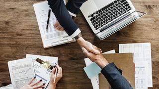 Two men shaking hands across a corporate desk 