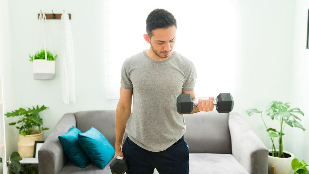 Man performs single dumbbell biceps curl at home