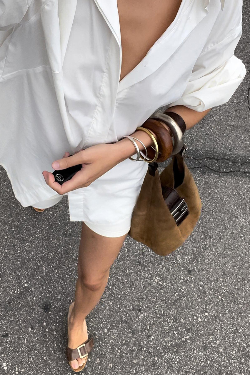 a woman wearing a white button-down, a suede bag, and stacked bracelets