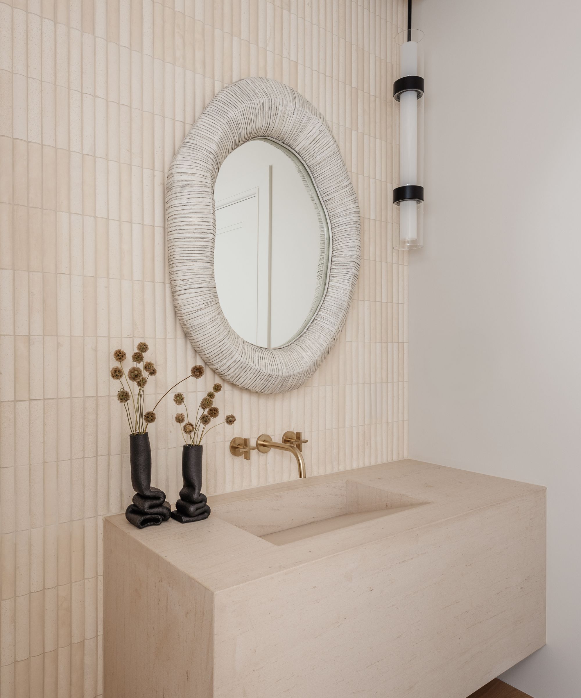 Powder room with neutral tiles and a stone sink with a textured mirror above and a black pendant lighting fixture hung to one side