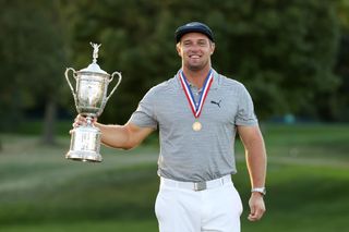 Bryson DeChambeau holds up the 2020 US Open trophy with one hand out to the side