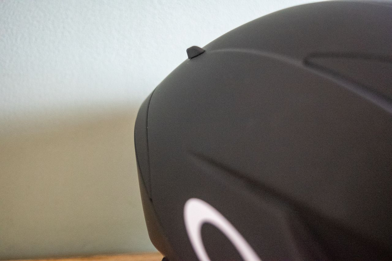 A rider wearing a black Oakley Velo Mac helmet in front of a green wall