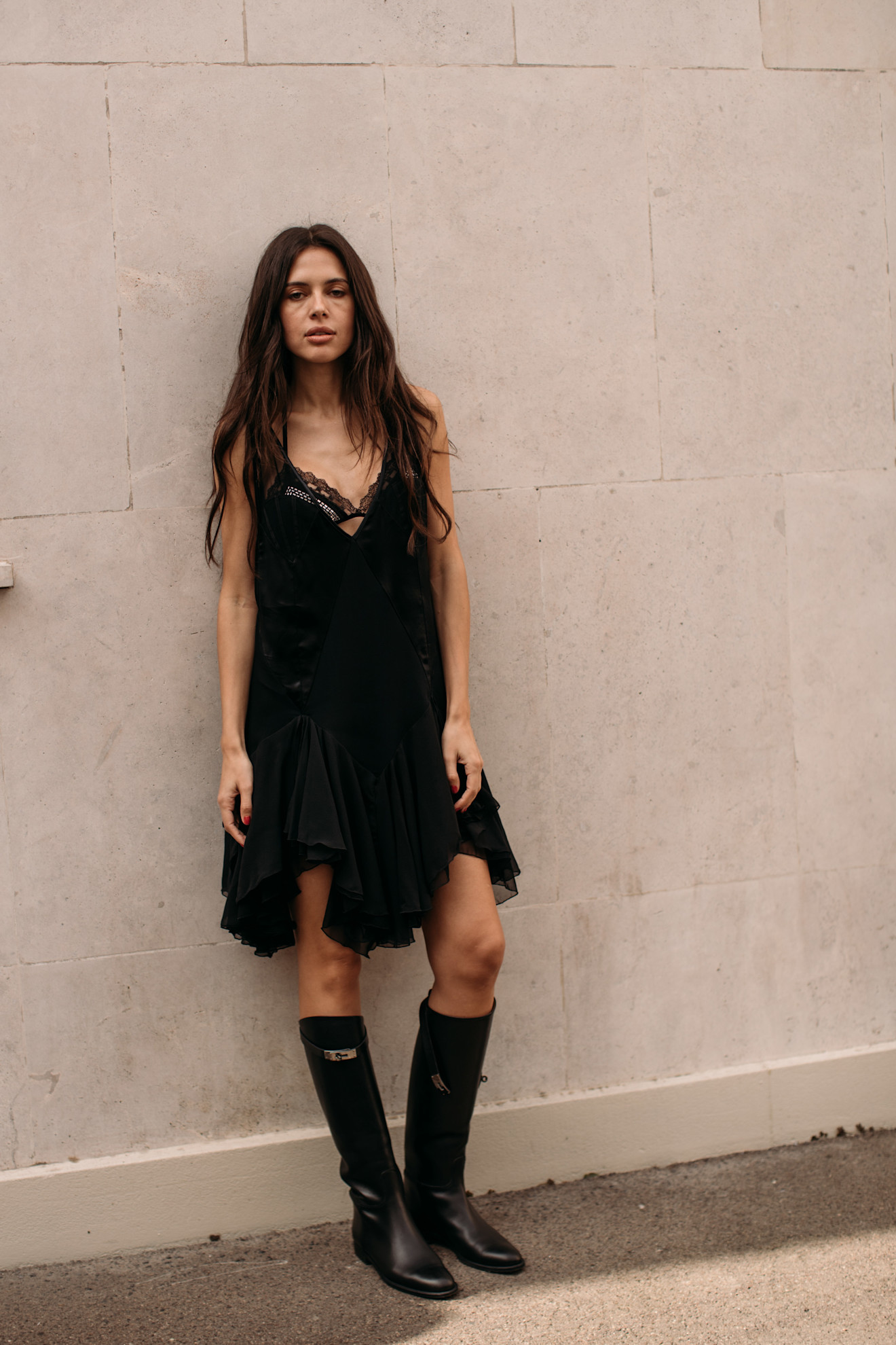 a woman at paris fashion week wearing a black dress and black riding boots