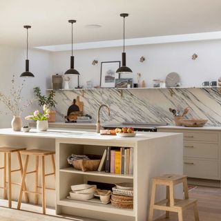 cream kitchen with large kitchen island with wooden stools and marble splashback and black pendant lights