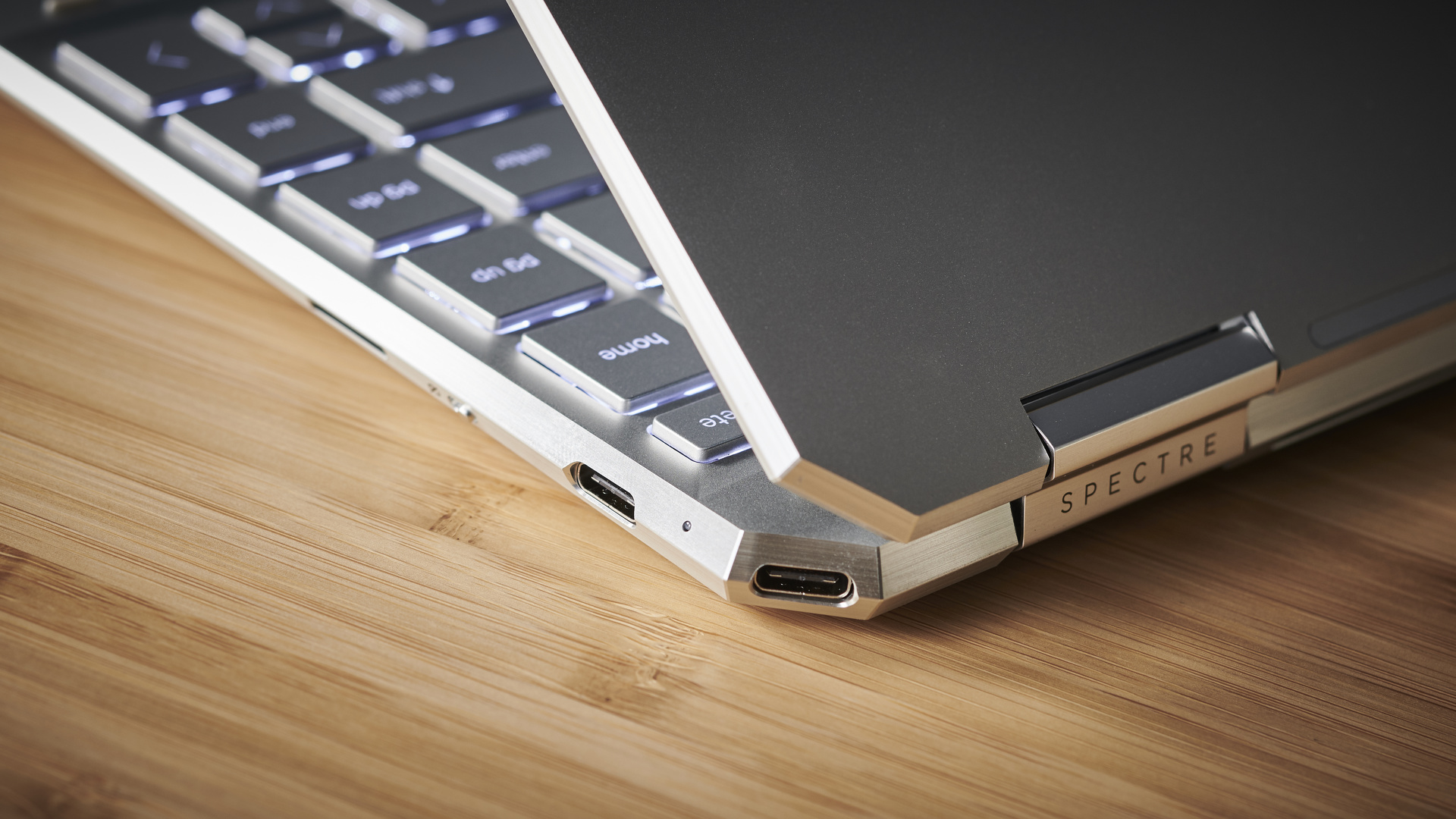 HP Spectre x360 (2021) on a wooden desk showing off its ports, its hinge, and part of its keyboard